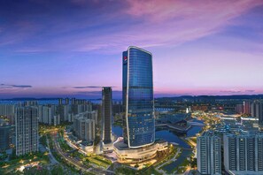 Un moderno edificio de gran altura con un diseño curvo único, rodeado de otros rascacielos y un río.