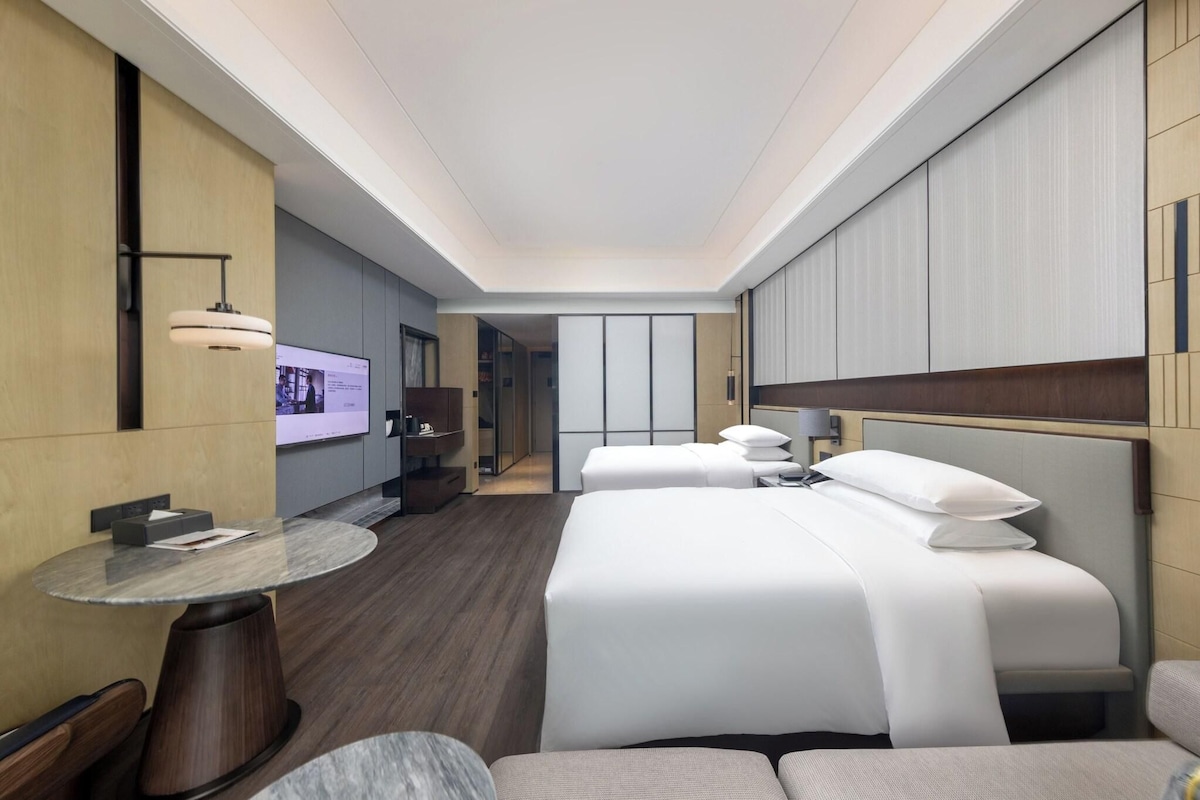 Una habitación de hotel moderna con una cama grande, una mesa redonda y un televisor en la pared.