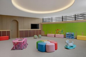 Une salle de jeux pour enfants avec une table rose, des tabourets colorés et un cheval à bascule blanc.