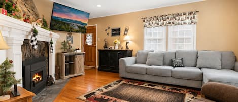 A living room with a fireplace, a sofa, a rug, and a wall with framed photos.