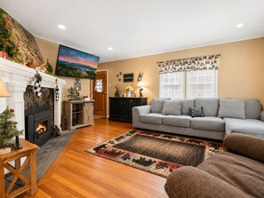 A living room with a fireplace, a sofa, a rug, and a wall with framed photos. - Country Bear Inn (Big Bear City)