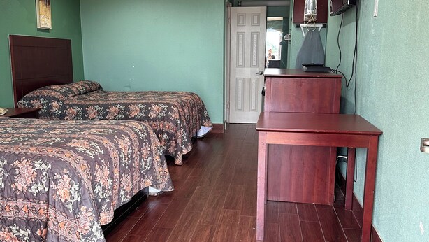 A room with two beds, a wooden desk, and a mirror on the wall. - Roadside Inn (Floresville)