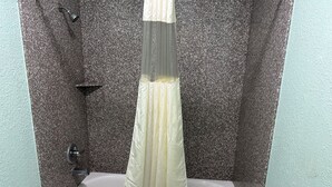 A bathroom with a granite wall, a white sink, and a shower curtain. - Roadside Inn (Floresville)
