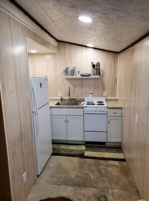 Eine kleine Küche mit Kühlschrank, Herd und Spüle, Holzwänden und einem Regal mit Küchenutensilien.