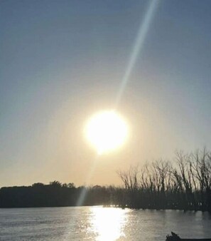 Ein Gewässer mit einer hellen Sonne, die tief am Horizont steht und sich auf der Oberfläche spiegelt.