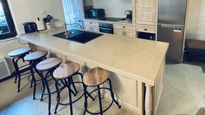 A kitchen with a large island, bar stools, a stainless steel refrigerator, and a microwave. - Historic Maison du Roy/Upper Chambers 3BR/2 BR Apartment with Balcony & View (Saint-Antonin-Noble-Val)