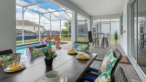 Eine überdachte Terrasse mit Blick auf einen Pool, Sitzgelegenheiten im Freien und eine Glastür zum Poolbereich.
