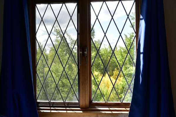 A window with a diamond-patterned grille, curtains, and a view of trees. - The Blue Cottage B&B (70 Mile House)
