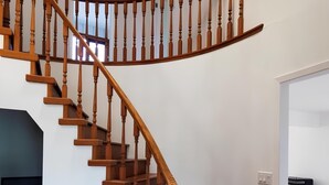 Un escalier en colimaçon en bois, avec un palier, une table en bois et un appareil électroménager noir en arrière-plan.