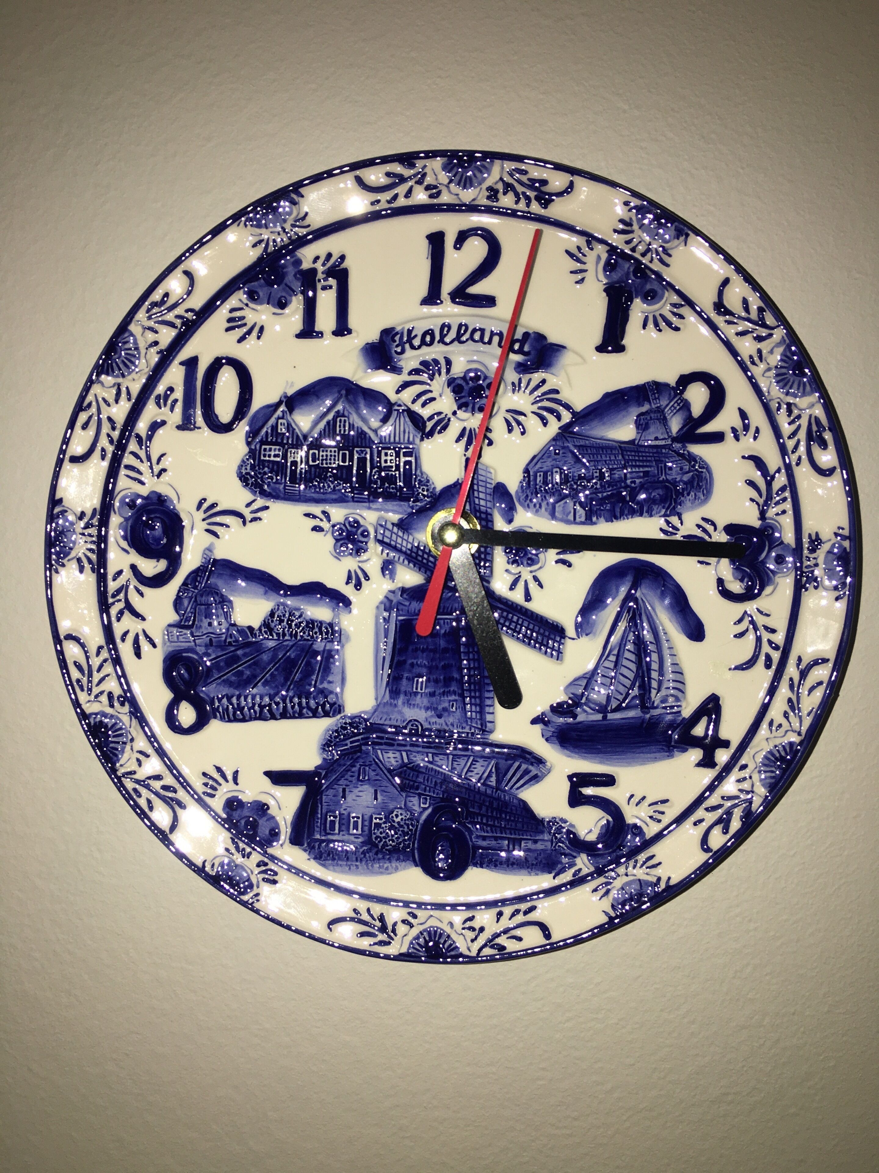A wall-mounted clock with a blue and white design featuring Dutch scenes and the word "Holland".