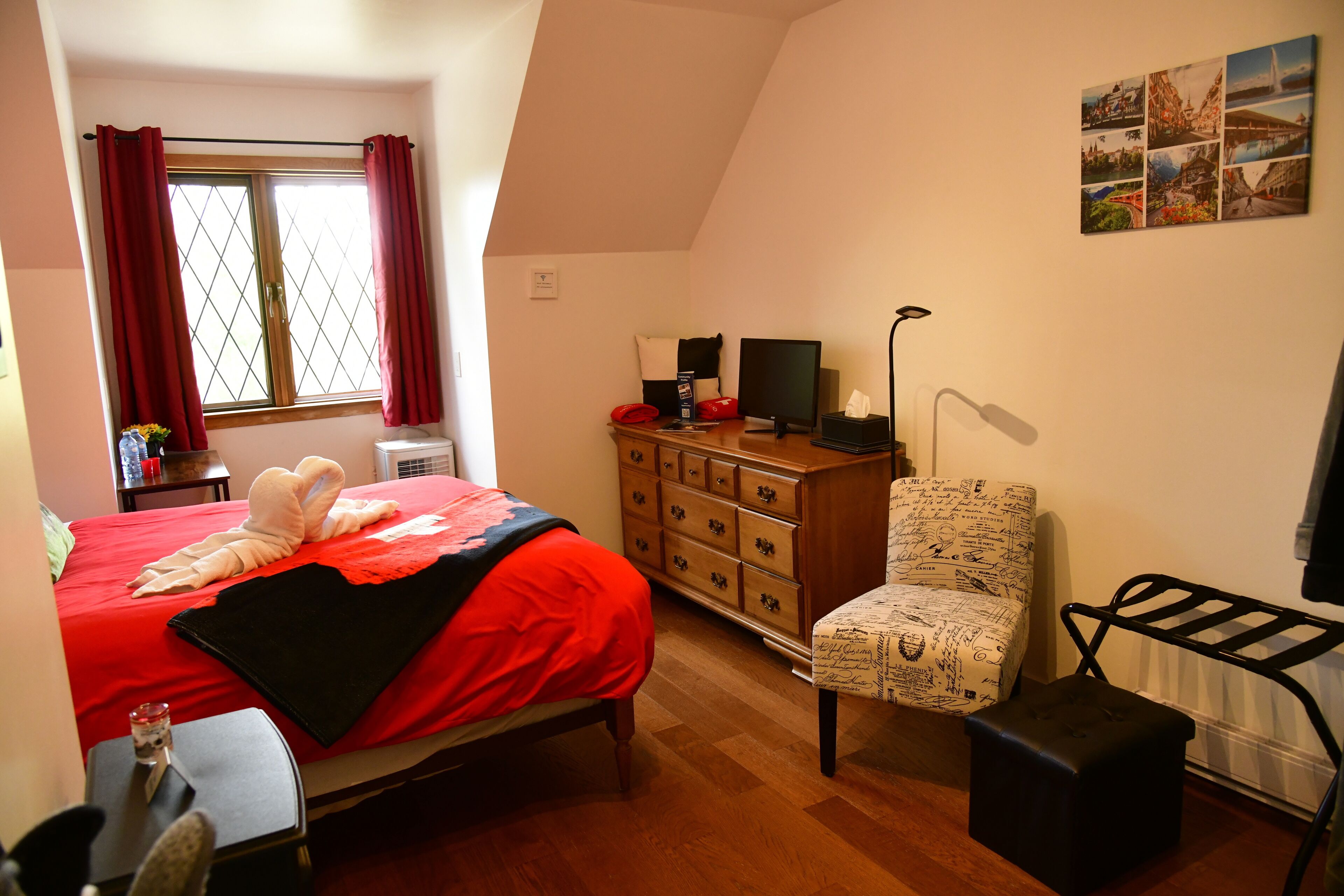A bedroom with a bed, dresser, chair, desk, lamp, and a window with curtains.