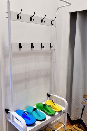 A white metal rack with multiple hooks and a shelf holding colorful slippers.