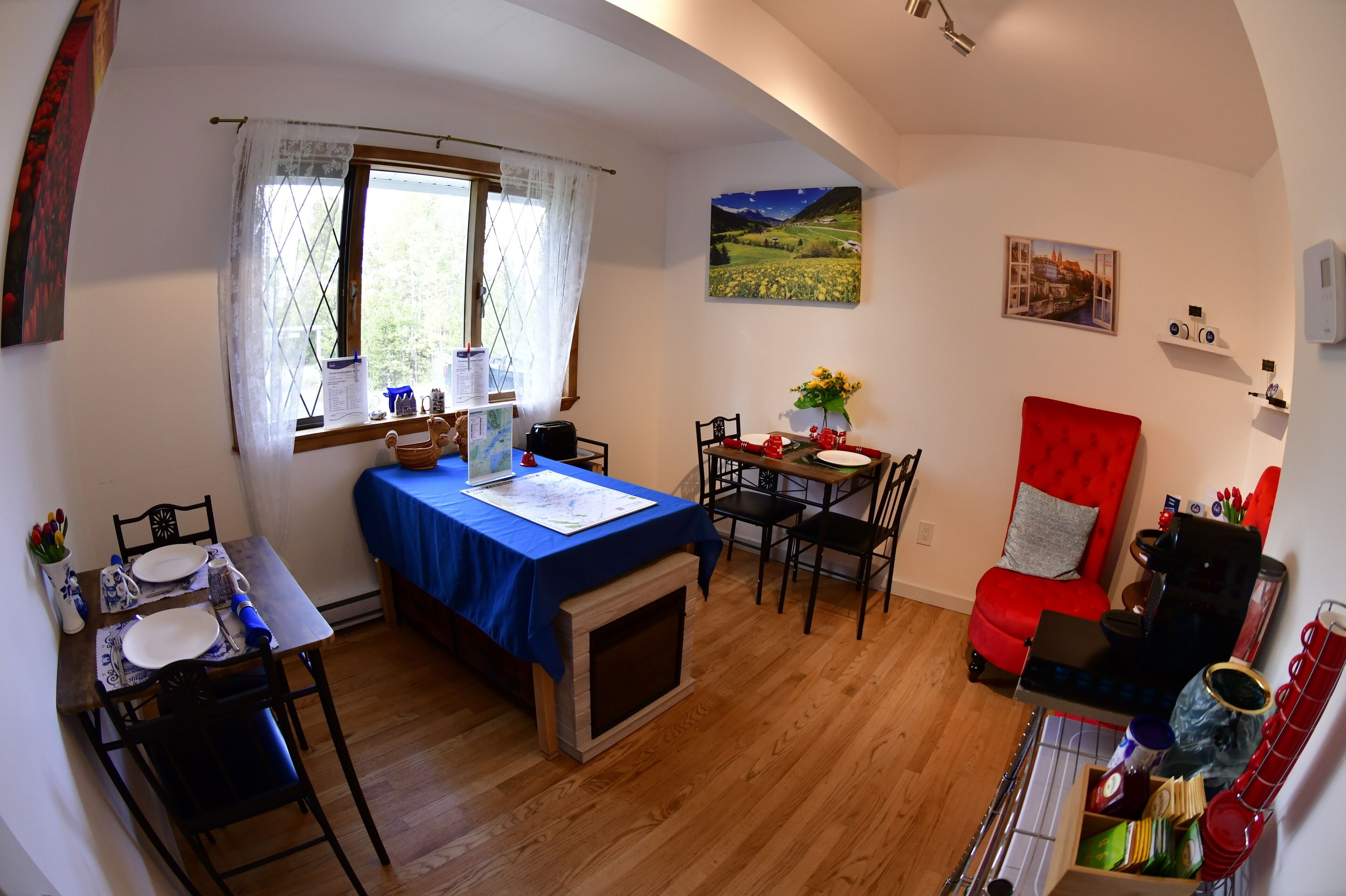 A cozy room with a dining table, a red armchair, a fireplace, and a window with a view of a field.