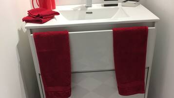 Une salle de bain avec un lavabo blanc, des serviettes rouges, un tapis rouge et une poubelle.