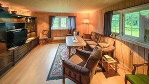 A cozy cabin interior with a dining table, sofa, and chairs, wooden walls, and a window with curtains. - Nice home in Sagstua with lake view (Sagstua)