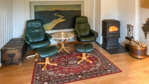 A cozy living room with two green leather chairs, a small round table, a red patterned rug, and a wood-burning stove. - Nice home in Sagstua with lake view (Sagstua)