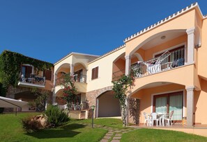 Ein mehrstöckiges Hotel mit Balkonen, Außenbestuhlung und einem steinernen Bogen.