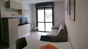 Un espacio habitable compacto con kitchenette, un sofá, una mesa de comedor y un televisor.