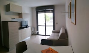A modern living space with a sofa, a TV on a cabinet, a dining table, and a sliding glass door.