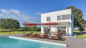 Una casa moderna con piscina, mobiliario exterior y un patio.