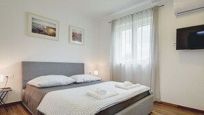 Habitación de hotel moderna con una cama grande, dos cuadros en la pared, un televisor de pantalla plana y piso de madera.