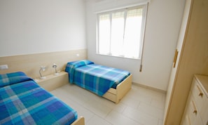 Quarto com duas camas, uma janela, mesa de cabeceira e guarda-roupa.