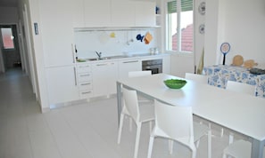 A modern kitchen with white cabinets, a dining table with chairs, and a window with a view of a red-roofed building.