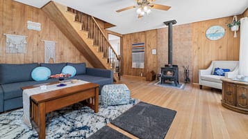 A cozy living room with a wooden staircase, a fireplace, and a ceiling fan.