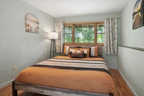 Ein Schlafzimmer mit Bett, einem Fenster mit Vorhängen, einer Stehlampe und einem Wandbild.