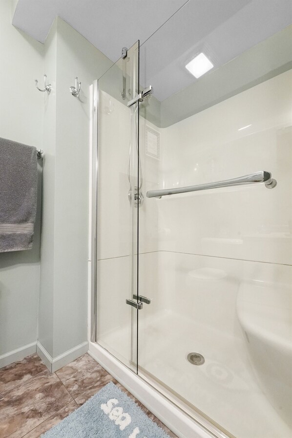 A modern bathroom with a glass shower enclosure, a white sink, and a towel rack.