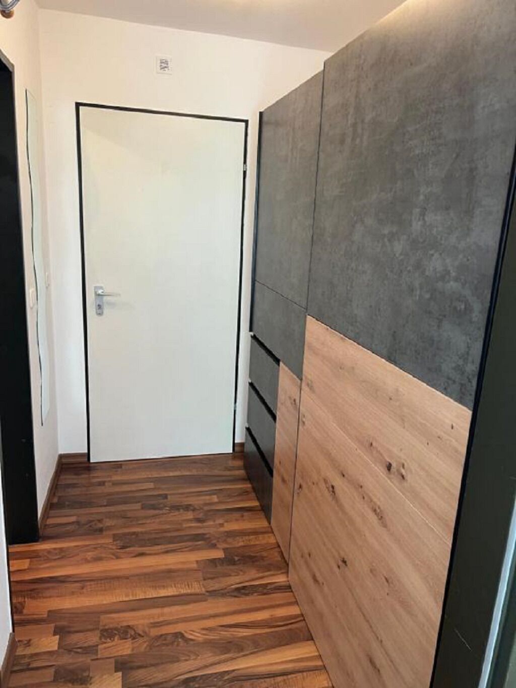 A hallway with a wooden floor, a white door, and a wall with a combination of grey and wooden panels.