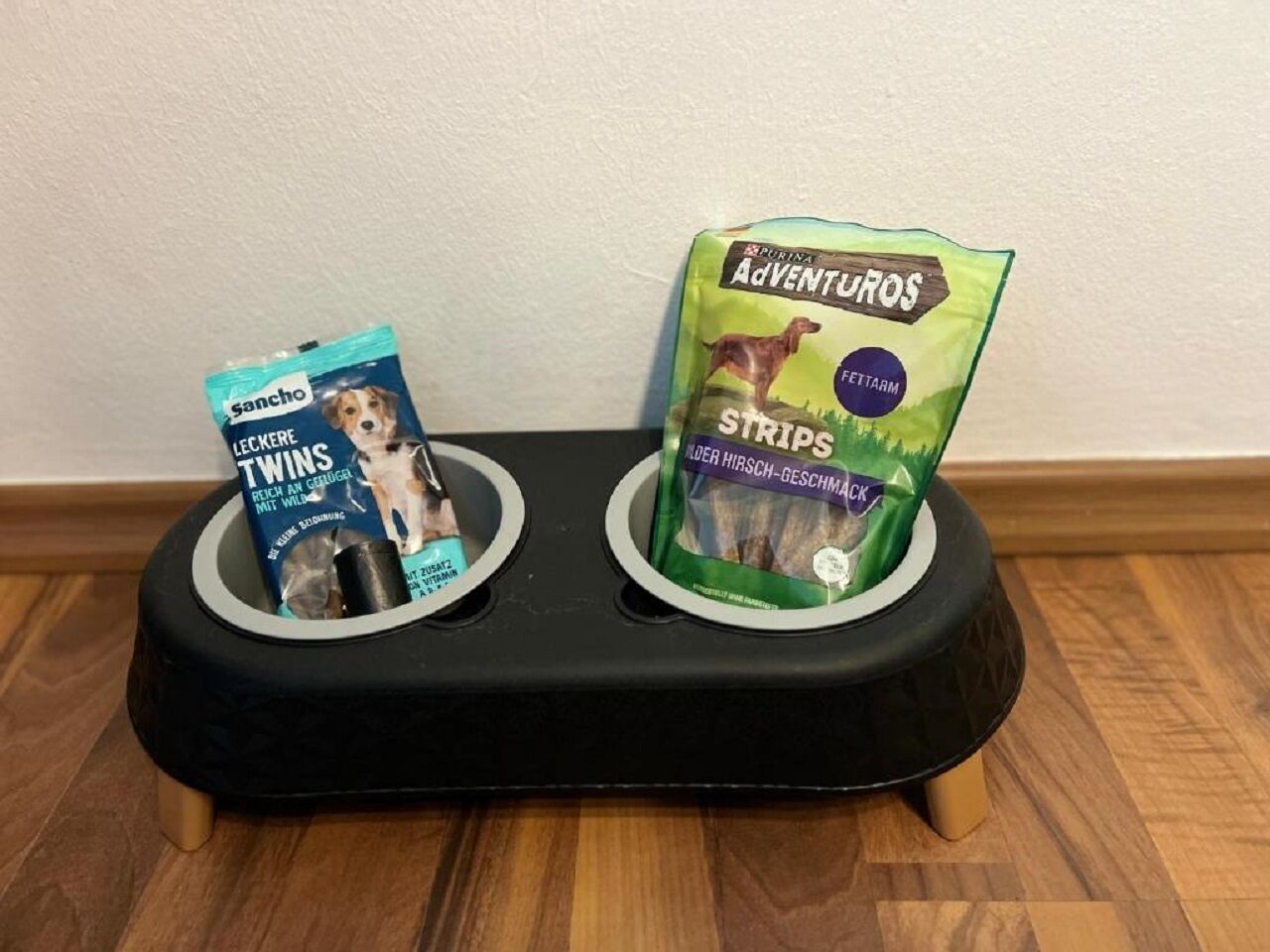 Un comedero negro para mascotas con dos compartimentos, cada uno conteniendo una bolsa de alimento para perros.