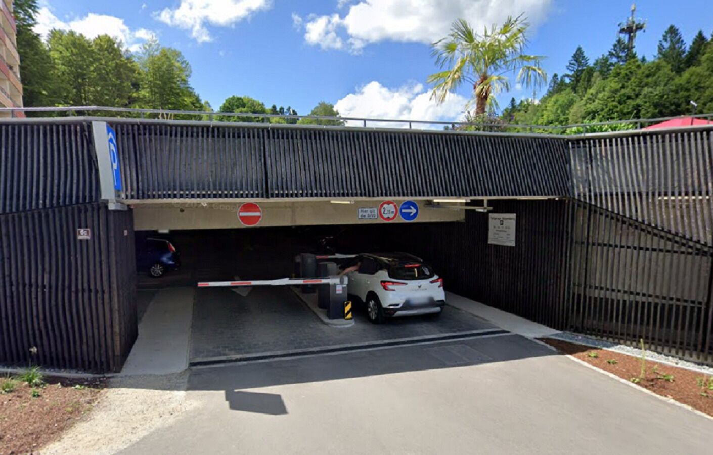 A gated parking area with a white car inside, a no-entry sign, and a directional sign indicating a 2-lane road.