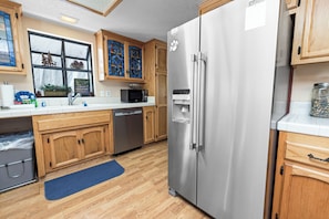 A kitchen with wooden cabinets, stainless steel appliances, and a blue rug. - Mount Bearadise (Big Bear City)