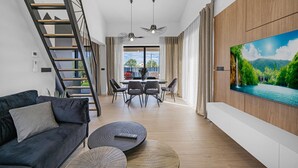 Ett modernt vardagsrum med en soffa, ett soffbord, en TV och en matplats med stolar och ett bord.