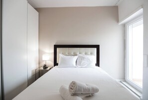 A hotel room with a large bed, a nightstand with a lamp, and a window.