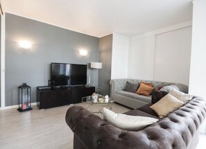 Uma sala de estar moderna com uma TV de tela plana, um sofá marrom escuro e um sofá cinza com detalhes em botão.