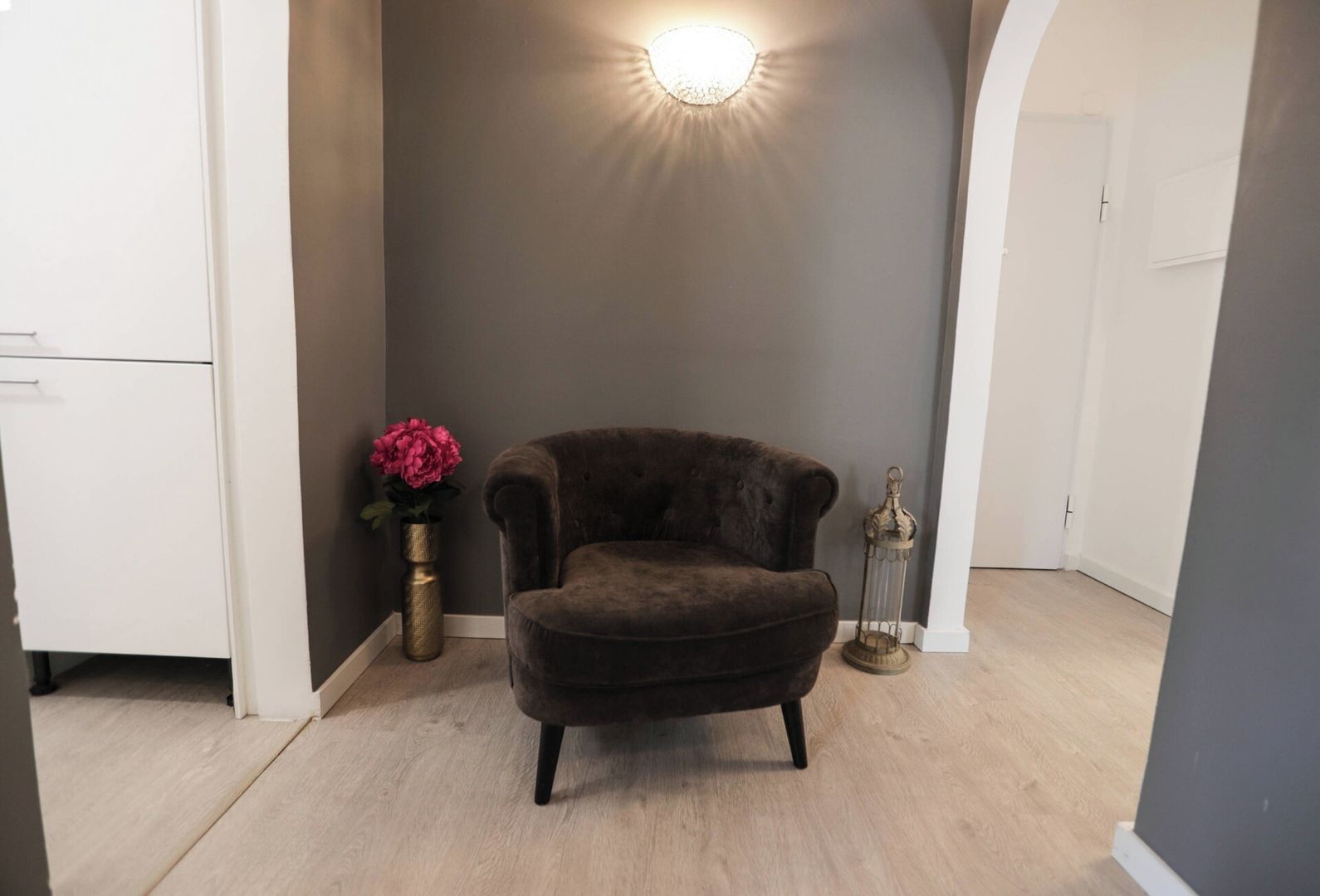 Ett rum med en mörkbrun fåtölj, en vas med rosa blommor och en dekorativ lampa.