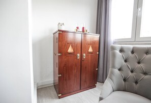 A wooden wardrobe with two doors, a grey upholstered armchair, and a window with curtains.