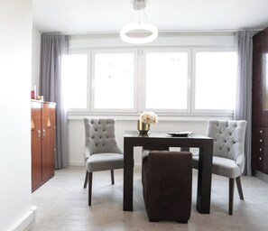 Uma sala de jantar moderna com mesa, duas cadeiras, um armário e uma janela grande com cortinas.