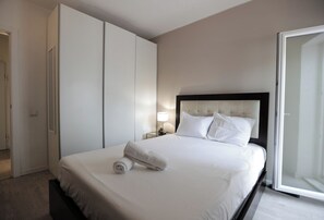Quarto de hotel com cama, mesa de cabeceira, abajur e porta deslizante.