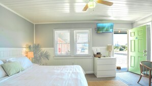 A bedroom with a bed, a nightstand, a lamp, a television, and a green door.