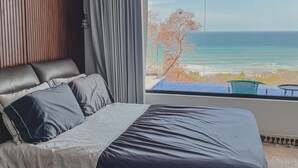 A bedroom with a large window offering a view of the ocean.