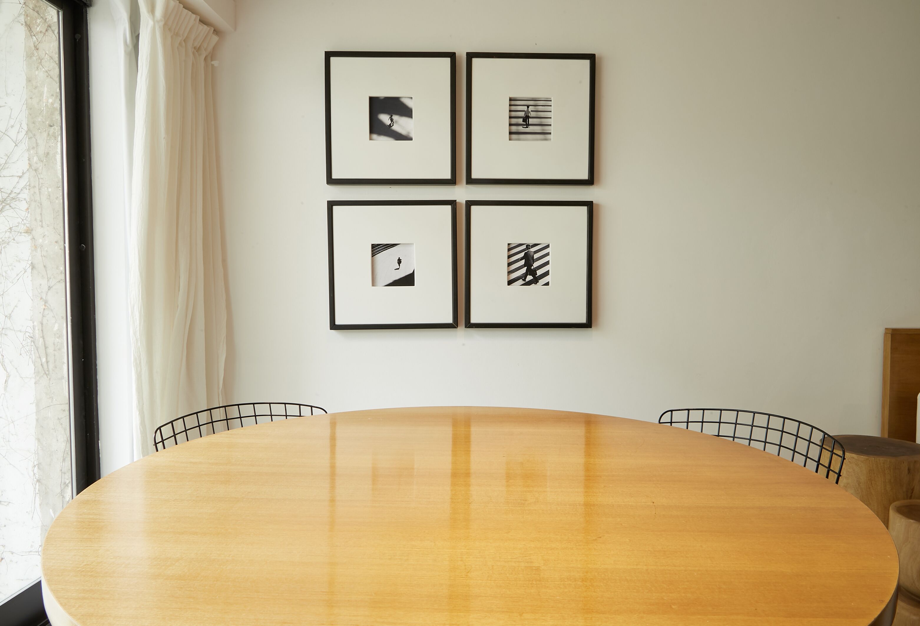 Ein runder Holztisch mit vier Stühlen, ein Fenster mit Vorhängen und vier gerahmte Bilder an der Wand.