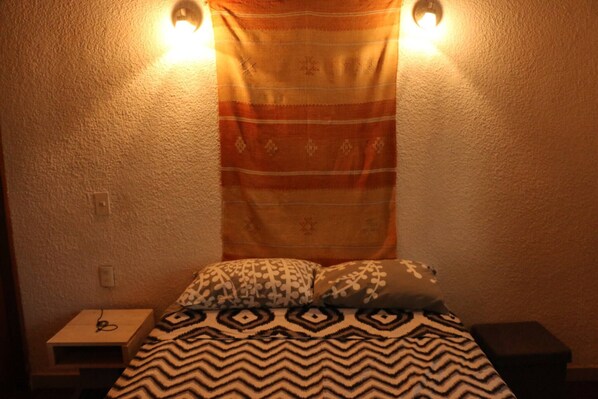 Cozy retreat with a patterned bedspread and geometric pillows, a wall-mounted light fixture, and a convenient nightstand.