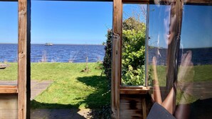 A wooden cabin with a large window offering a view of a body of water and a distant pier. - Waterfront Holiday Home Sonnenschein 4 Persons With Sauna (Anjum)