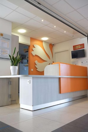 A reception desk with a modern design, a potted plant, and a wall-mounted television.