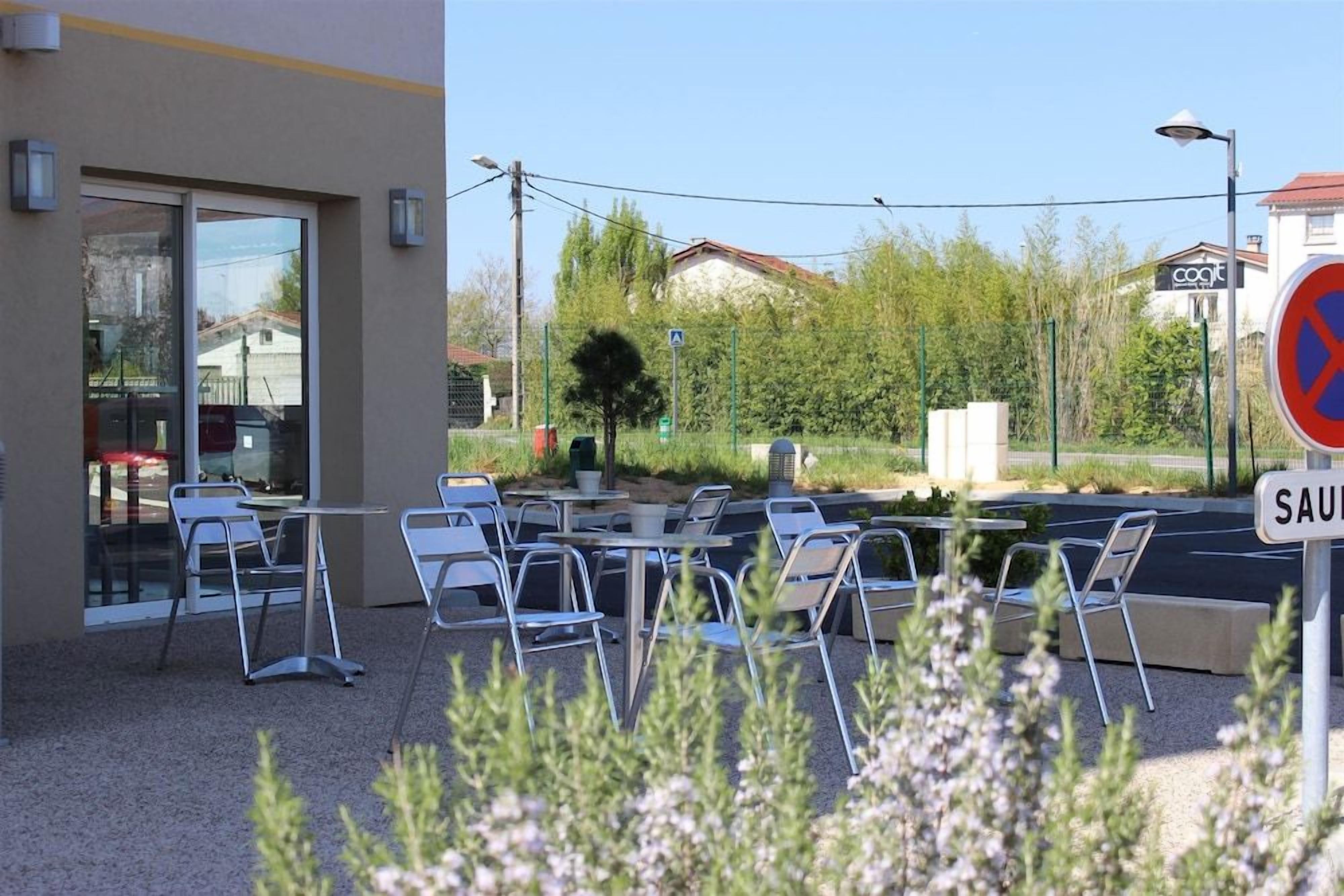 Een terras met tafels en stoelen, een gevelingang en een parkeerverbodsbord.