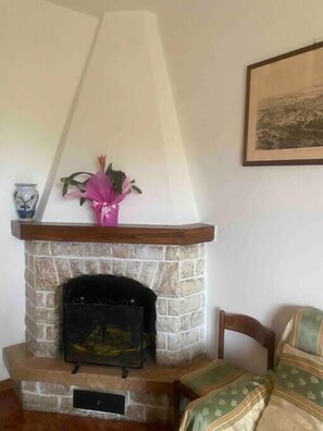 A stone fireplace with a mantel, a pink flower arrangement, and a framed picture on the wall. - Siena-crete Senesi-val Dorcia (Asciano)