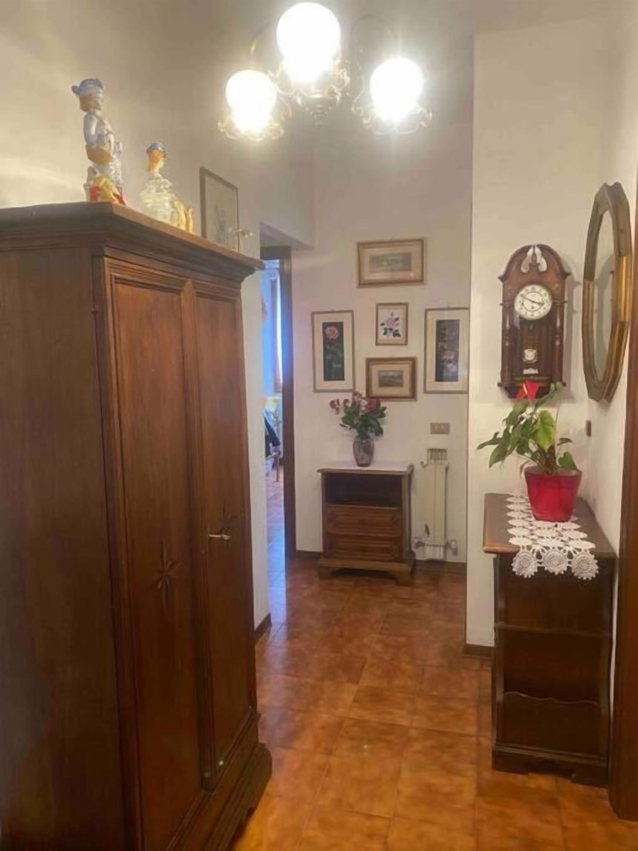 A hallway with a wooden wardrobe, a clock, framed pictures, and a potted plant.